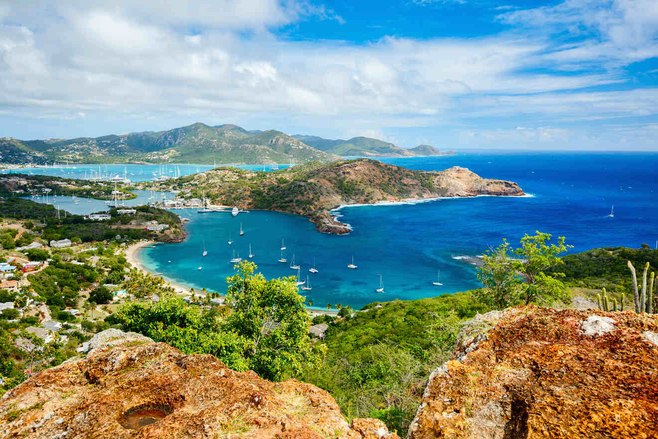 Panoramic view of a lush tropical coastline featuring multiple bays with turquoise waters and anchored sailboats, surrounded by green hills under a clear blue sky
