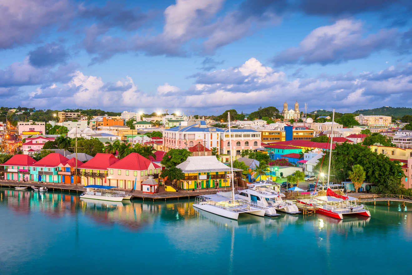 Aerial view of a vibrant Caribbean town at dusk, showing colorful waterfront buildings and moored boats in the harbor with a backdrop of rolling hills and patchy clouds in the sky