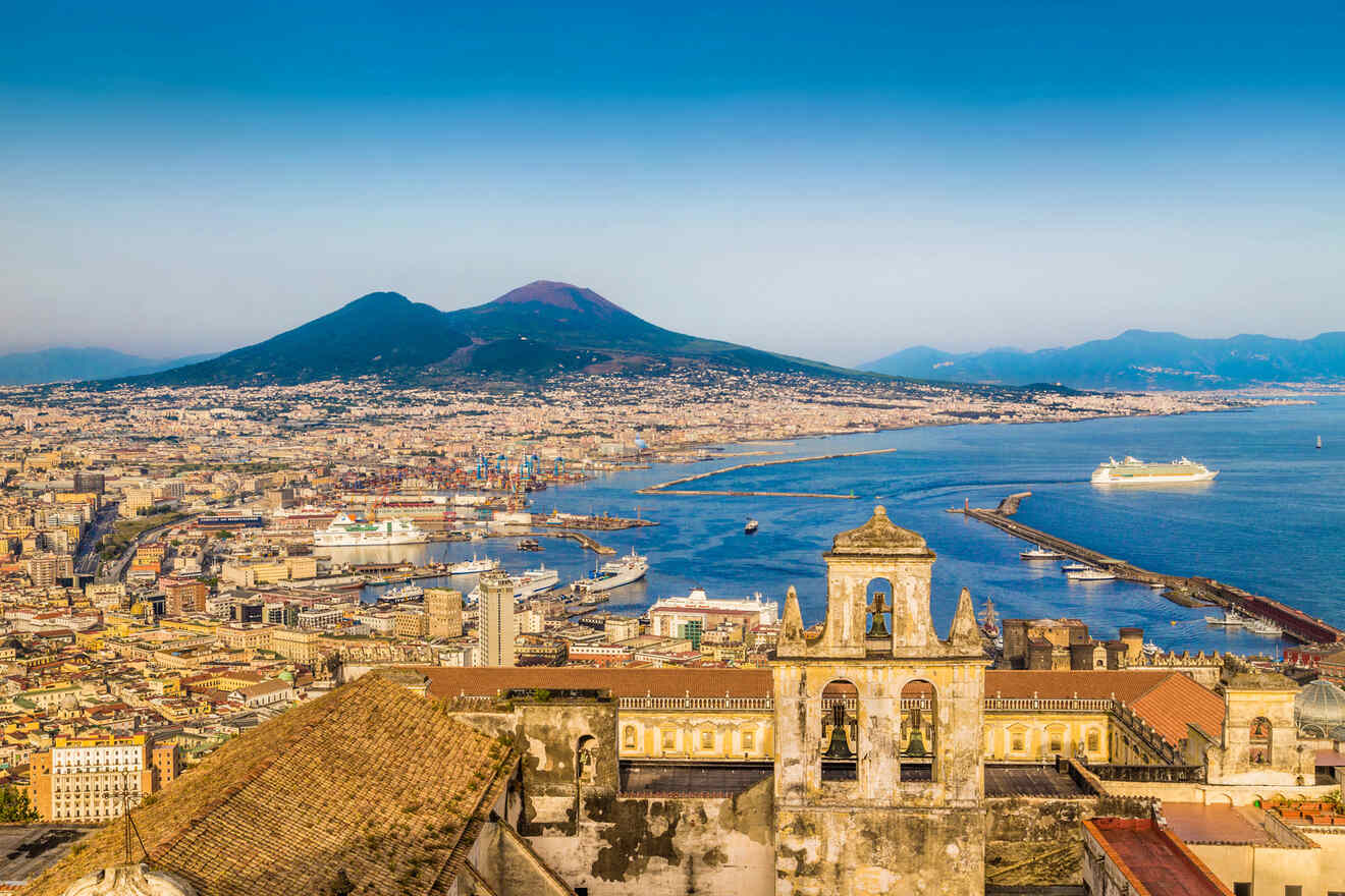 A panoramic view of Naples, Italy, featuring Mount Vesuvius in the background, the city's urban landscape, the harbor, and a large cruise ship docked by the coastline.