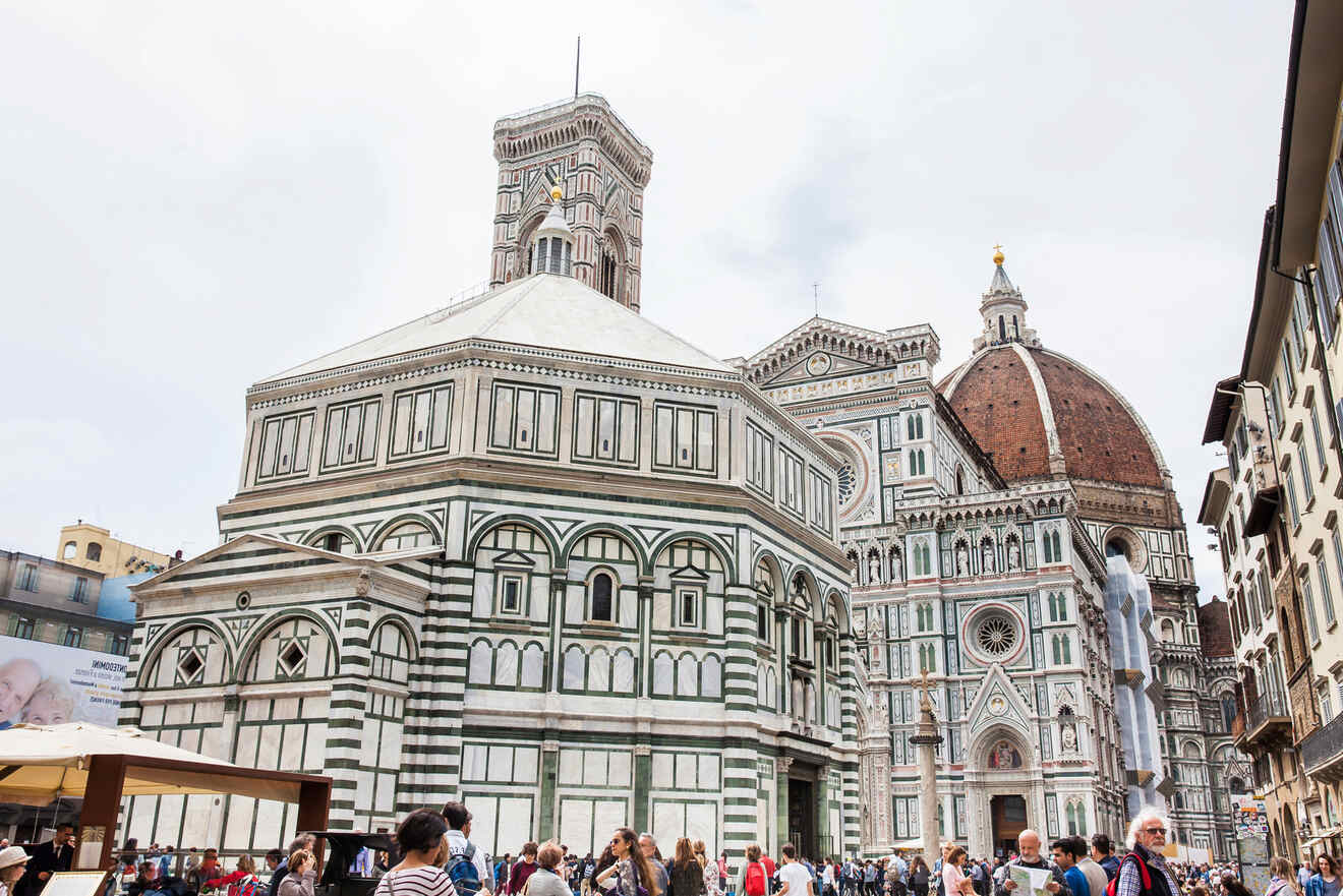 A crowd of people stands outside the Florence Cathedral, featuring its iconic dome and the adjacent octagonal Baptistery with its intricate façade.