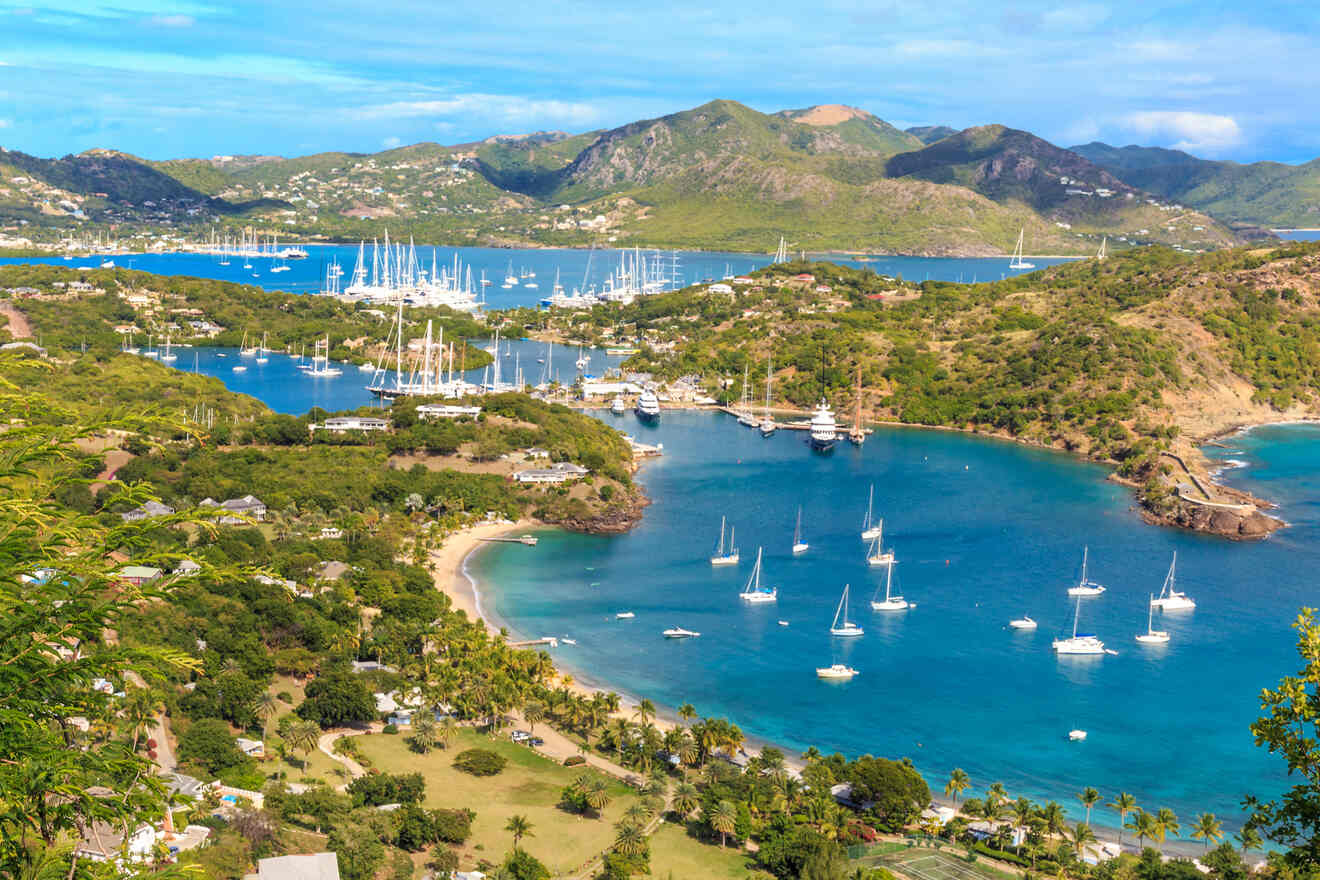 Breathtaking aerial view of a lush, tropical harbor with multiple bays filled with numerous sailing boats, surrounded by verdant hills and clear turquoise waters, under a partly cloudy sky
