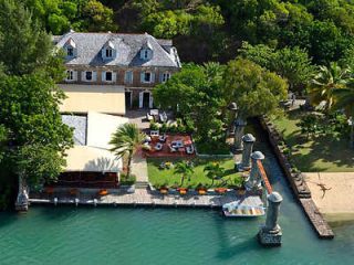 Aerial view of a colonial waterfront estate with lush gardens and a dining patio