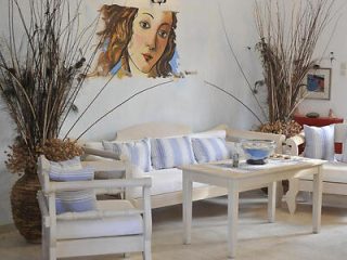 A living room with white furniture, a wooden coffee table, blue and white cushions, dried plant decorations, and a wall mural of a woman's face.