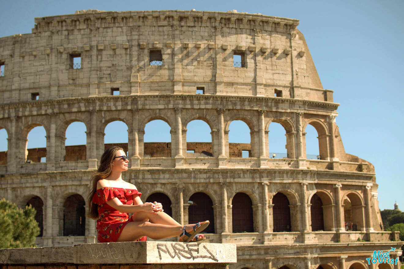 The writer of the post in a red dress sits in front of the Colosseum in Rome, enjoying the sunlight