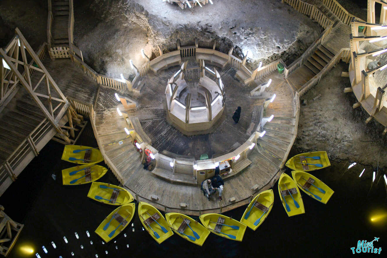 Aerial view of an underground wooden platform with a circular structure, surrounded by yellow boats on a dark water surface.