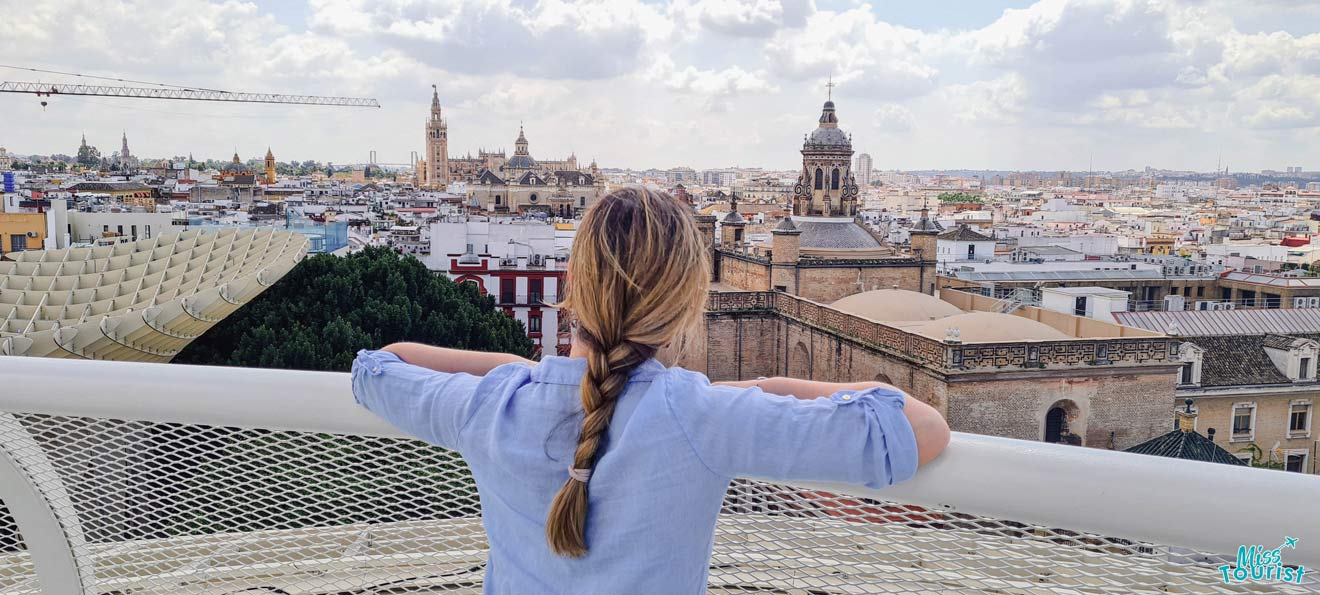 A panoramic view from the top of Metropol Parasol, offering a sweeping vista of Seville's skyline punctuated by the Giralda and Seville Cathedral, as seen over the shoulder of a person leaning on the enclosure