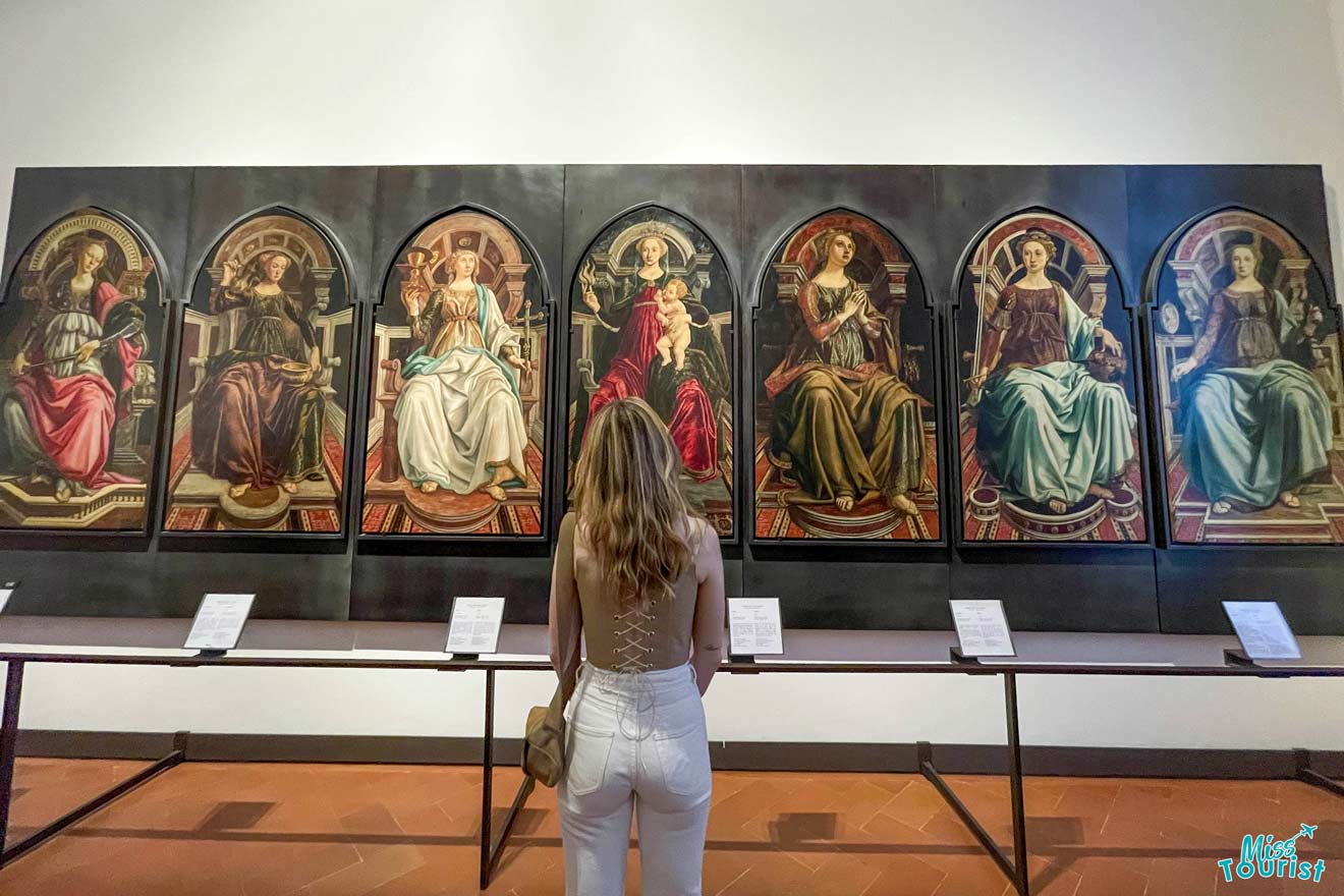 author of the post stands in front of a display of six framed paintings depicting various figures, observing the artworks. Information plaques are visible below each painting.