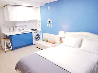 Stylish blue and white apartment with a bed, kitchenette, and washing machine.