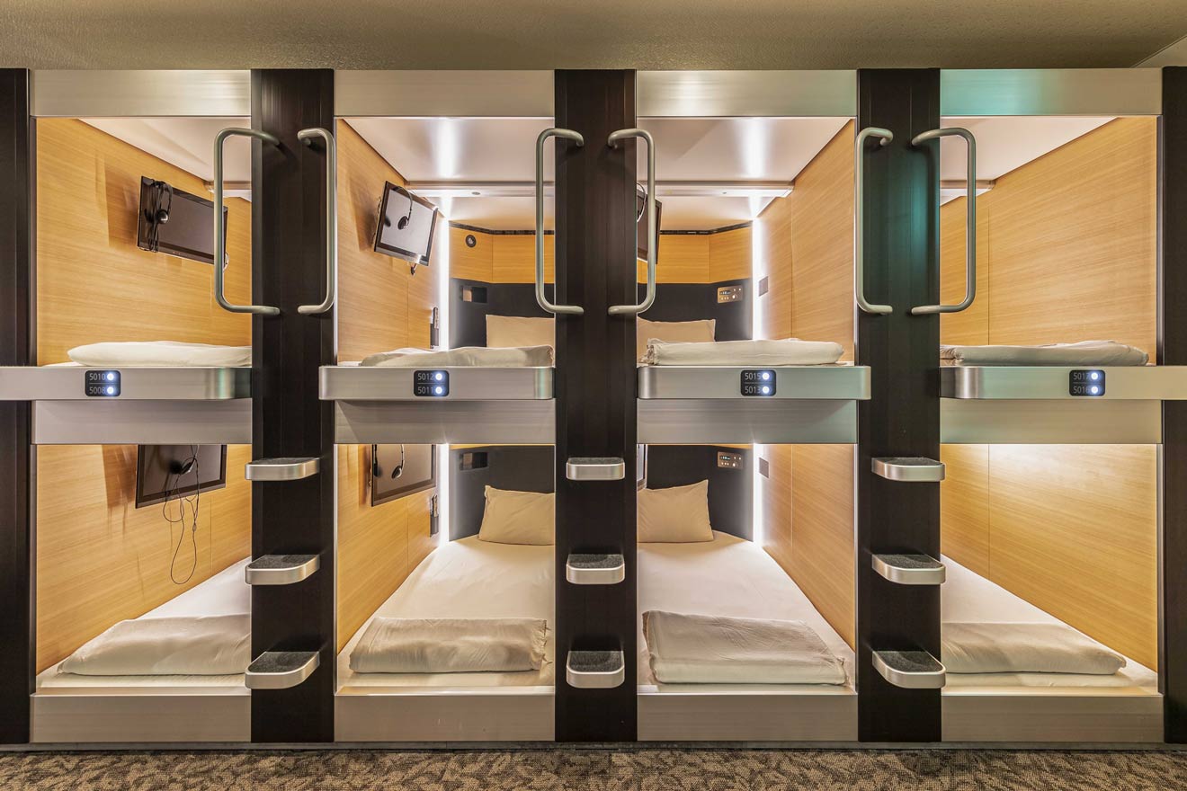 A modern capsule hotel room with well-organized, cozy sleeping pods equipped with individual lighting, electronics charging ports, and small television screens