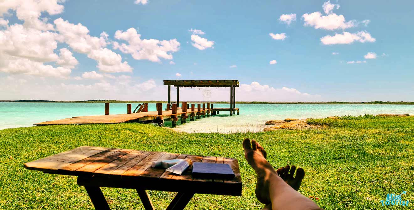 a person's feet resting on a picnic table near a body of water