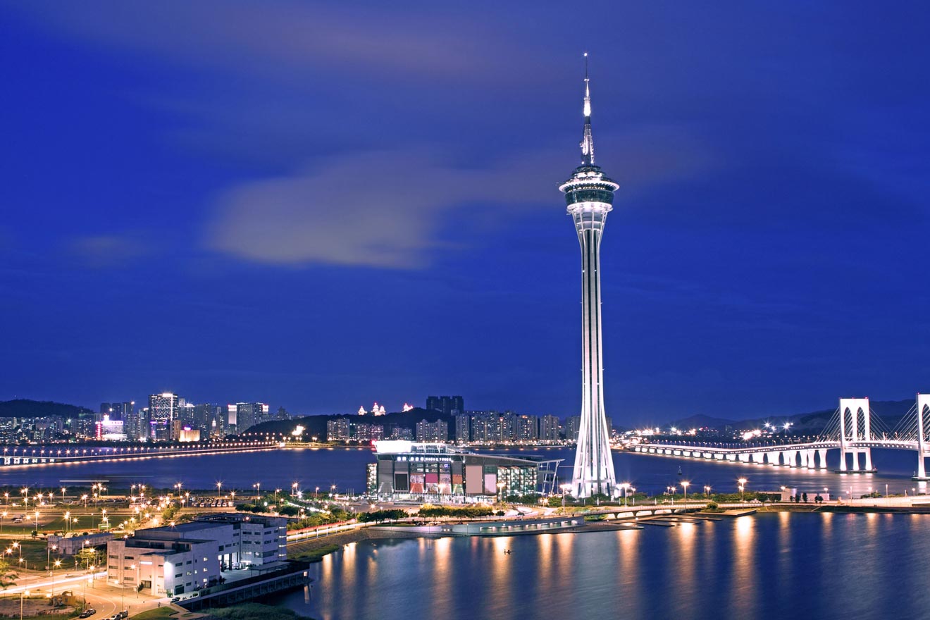 Night skyline of Macau with the Macau Tower standing tall above the illuminated cityscape and bridge reflecting in the water.