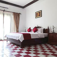 Traditional bedroom with white bedding, red accents, and checkerboard tiled flooring, evoking a classic elegance