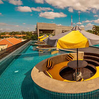 Rooftop pool with submerged circular seating area and yellow umbrellas, offering a cityscape view under a blue sky