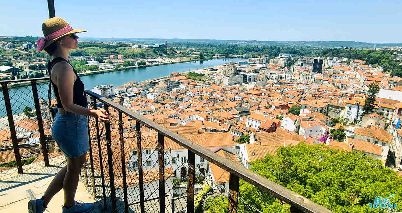 The writer of the post in a hat overlooks a city with red-roofed buildings and a river, from a high vantage point.