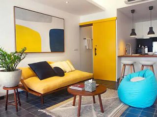 Modern living room with yellow sofa, blue bean bag chair, abstract wall art, and a potted plant