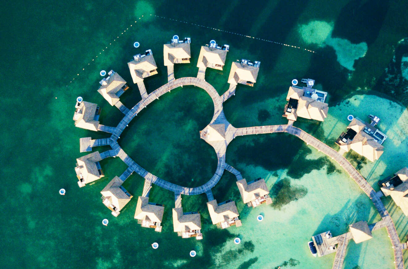 Aerial view of a heart-shaped arrangement of overwater bungalows connected by wooden walkways in a turquoise sea.