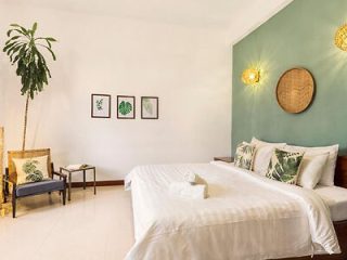 A bright and airy bedroom with white walls, featuring a teal accent wall behind the bed with plant-themed art and a circular wicker wall decor