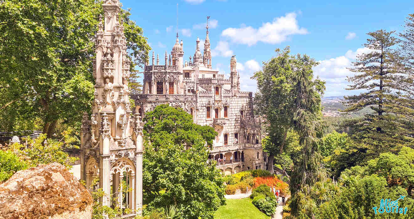 A breathtaking view of a gothic-style palace surrounded by lush gardens and tall trees, with intricate architectural details standing out under a bright blue sky.