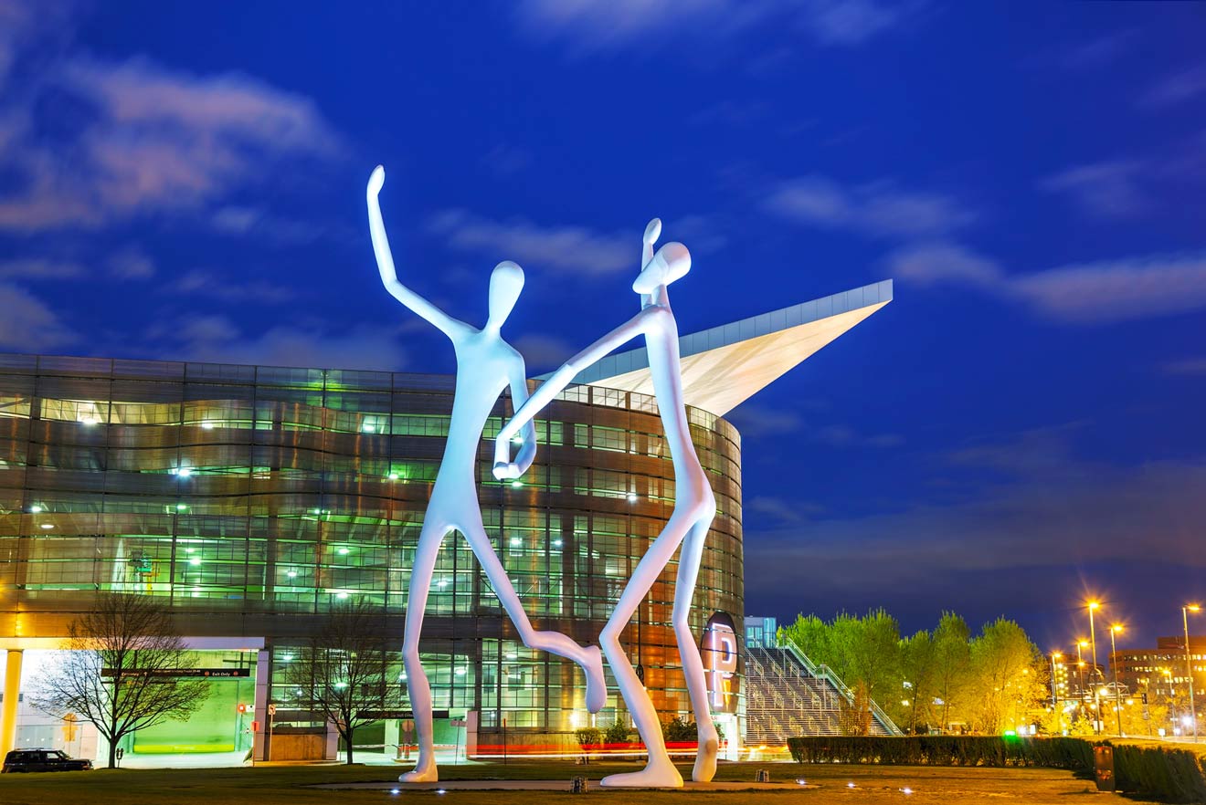 The 'Dancers' sculpture at the Denver Performing Arts Complex at night, with the building's illuminated facade creating a whimsical backdrop