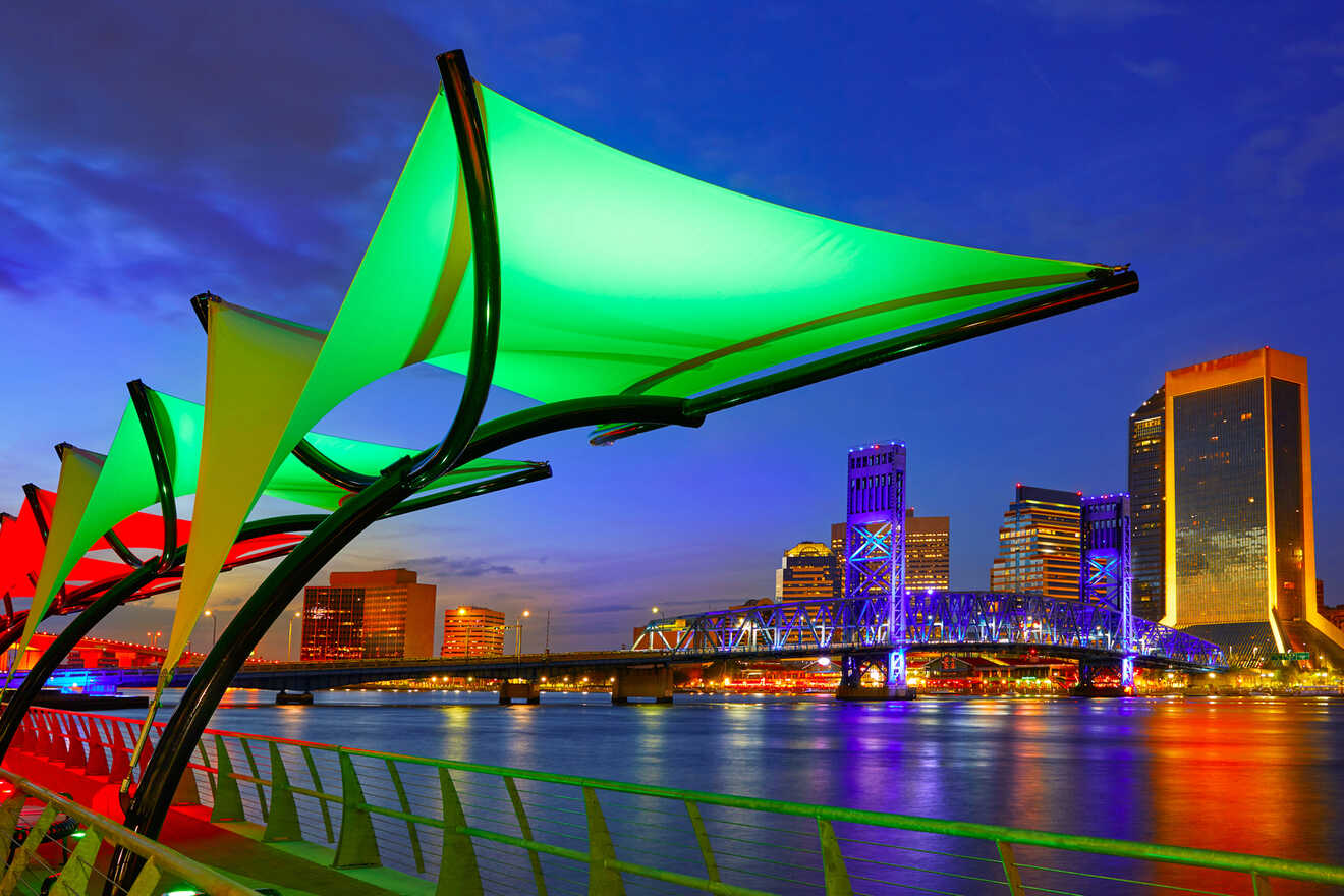 Colorful canopies and illuminated buildings reflect on a river at dusk, with a lit bridge in the background.