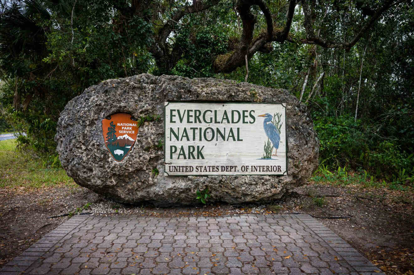 Stone sign for Everglades National Park, featuring the U.S. National Park Service emblem and a bird illustration, surrounded by trees.