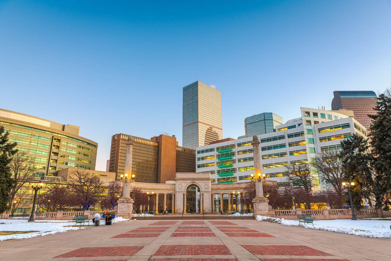 The Civic Center Park in Denver during twilight with snow patches on the ground, the Greek amphitheater and several high-rise buildings in the backdrop