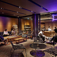 A modern lounge area with people sitting on couches and chairs, illuminated by warm purple lighting.