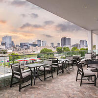 Outdoor terrace with high-top seating offering a panoramic view of a city skyline at dusk, under a spacious covered patio