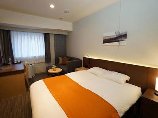 A hotel room with a large bed, orange bed runner, and a small seating area, designed for comfort and relaxation.