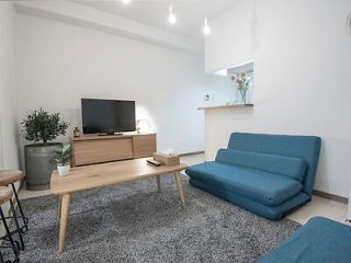 A minimalist living room with blue sofas, a wooden coffee table, and a flat-screen TV on a wooden stand.