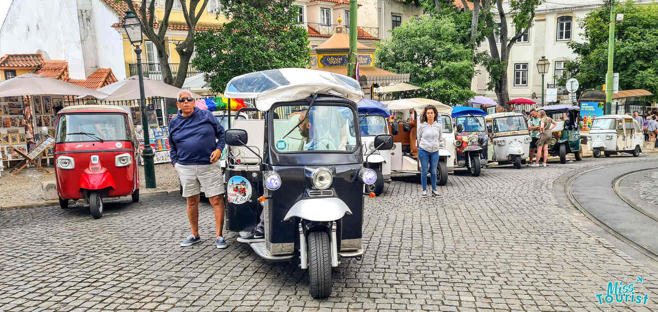 A row of parked tuk-tuks on a cobblestone street with a man standing next to the front one.