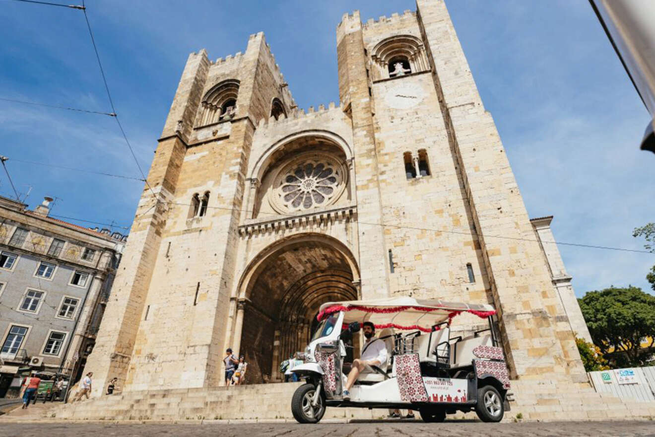 A tuk-tuk is parked in front of a large, historical cathedral with two bell towers and a rose window.