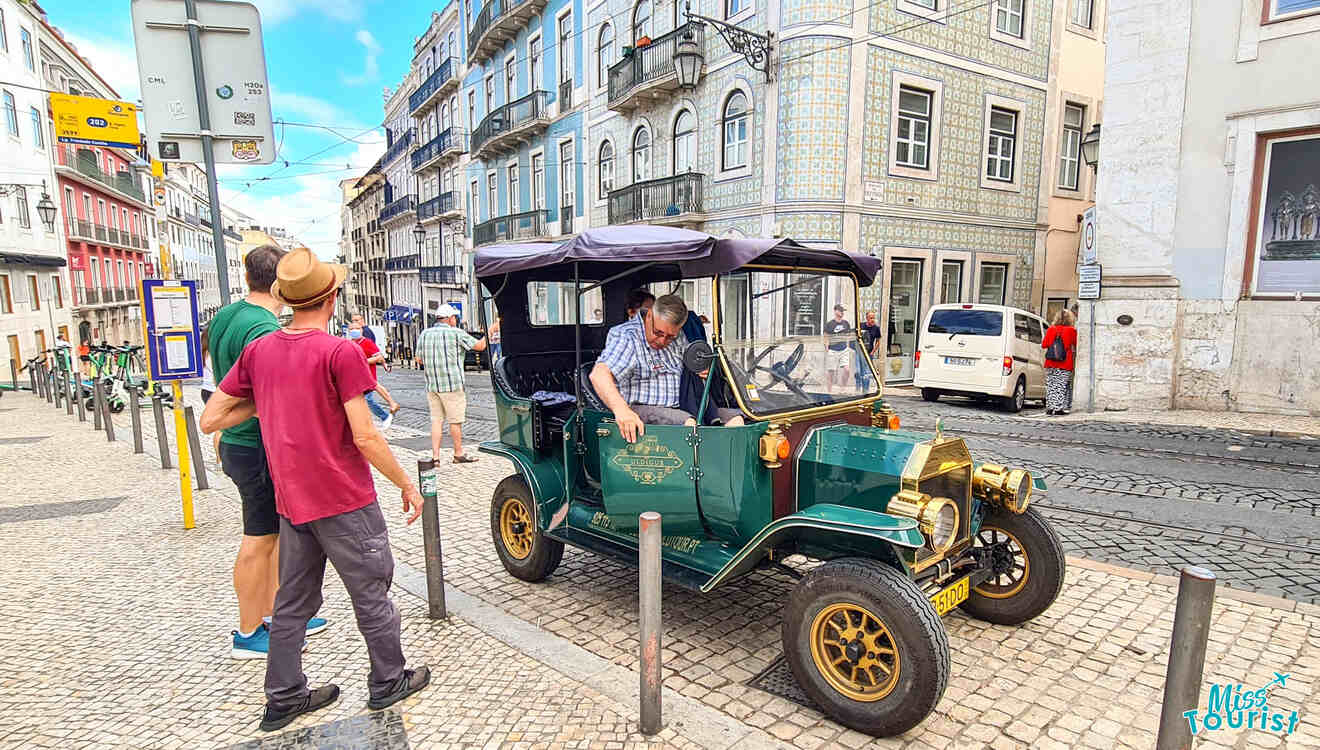 A vintage car parked on a cobblestone street in a European city. A man examines the vehicle while people walk nearby.