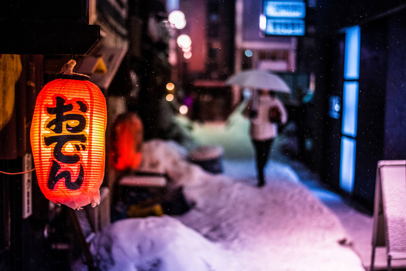 A vibrant night scene of a snow-covered street with a glowing red lantern and a person holding an umbrella.