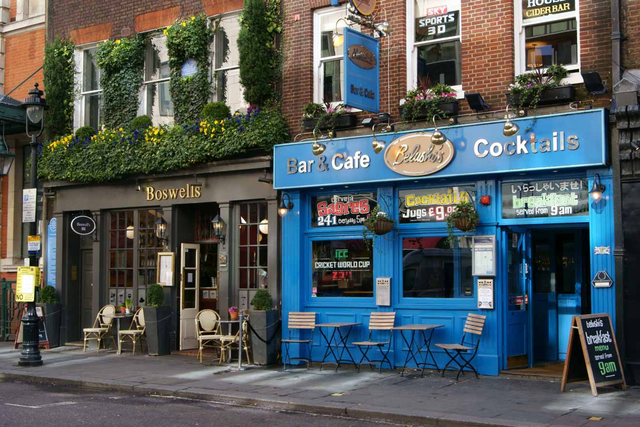 Side-by-side view of two establishments, Boswells and Cheers Bar & Cafe. Boswells has greenery on its facade, and Cheers has a blue exterior with outdoor seating.