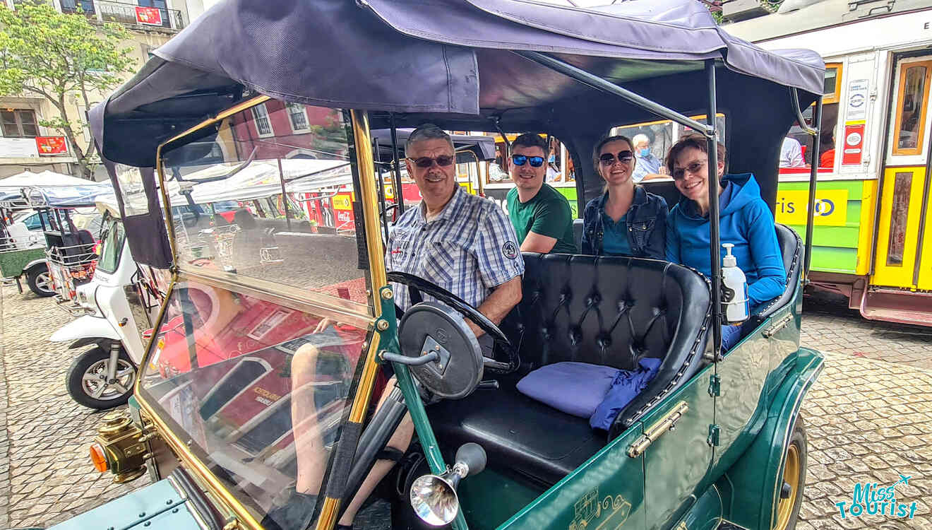 Four people sitting inside a vintage car, smiling at the camera. Street scenes and parked trams are visible in the background.