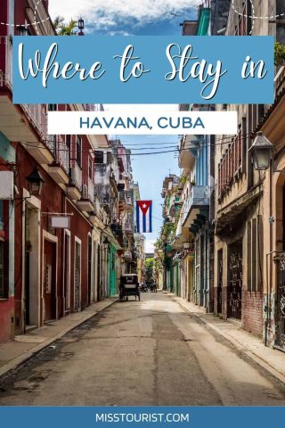 A narrow street in Havana, Cuba, lined with colorful buildings and balconies, with a Cuban flag hanging in the distance. Text reads "Where to Stay in Havana, Cuba" at the top.