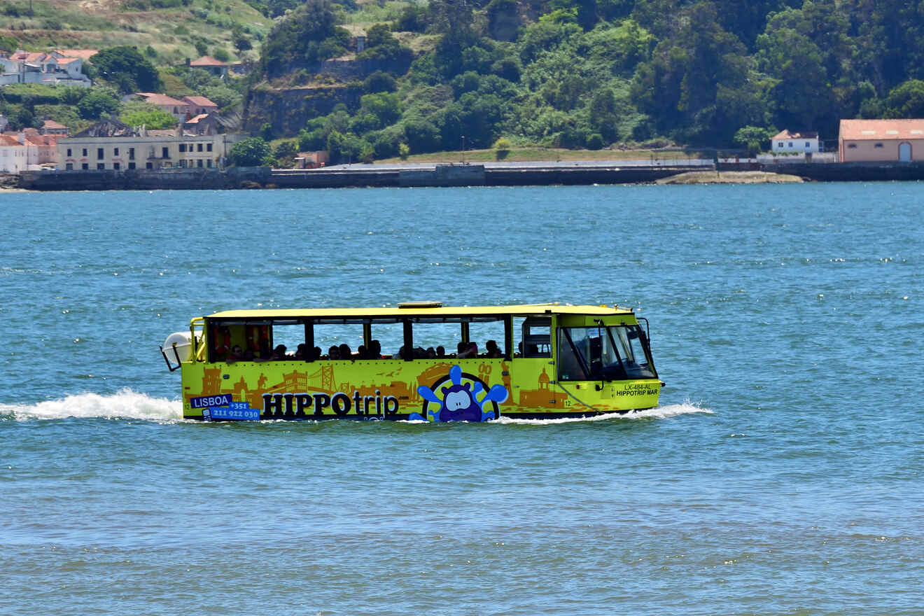 A bright yellow amphibious vehicle with "Hippotrip" branding moves through blue water with a shoreline and greenery in the background.