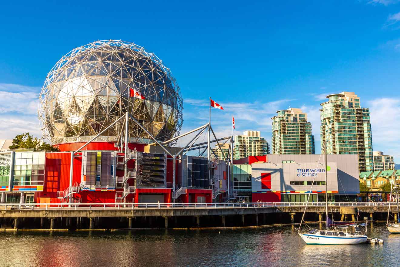 TELUS World of Science geodesic dome in Vancouver illuminated in daylight with Canadian flags and a clear blue sky.