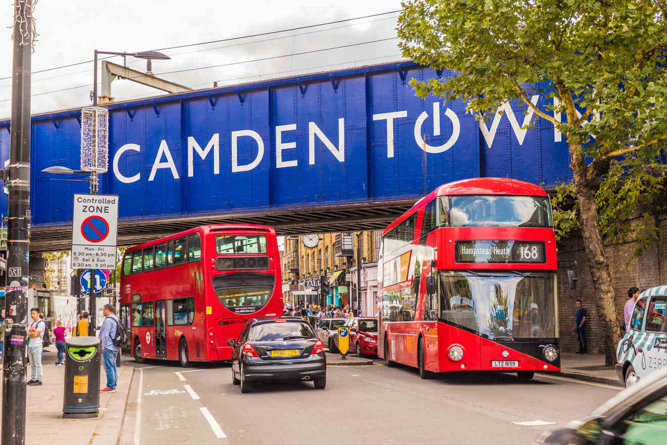 Camden Town railway bridge with two red double-decker buses and several cars on the road below. A sign reads "Controlled Zone." Trees partially block the view on the right.