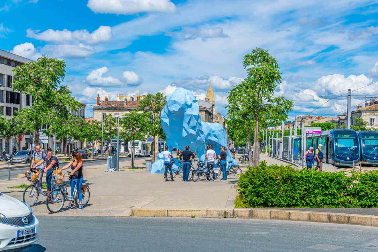 A group of people riding bicycles and standing around a blue lion statue in Bastide, Bordeaux.