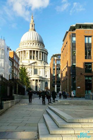 People walking near St. Paul’s Cathedral in London, with surrounding modern buildings and a clear blue sky in the background.