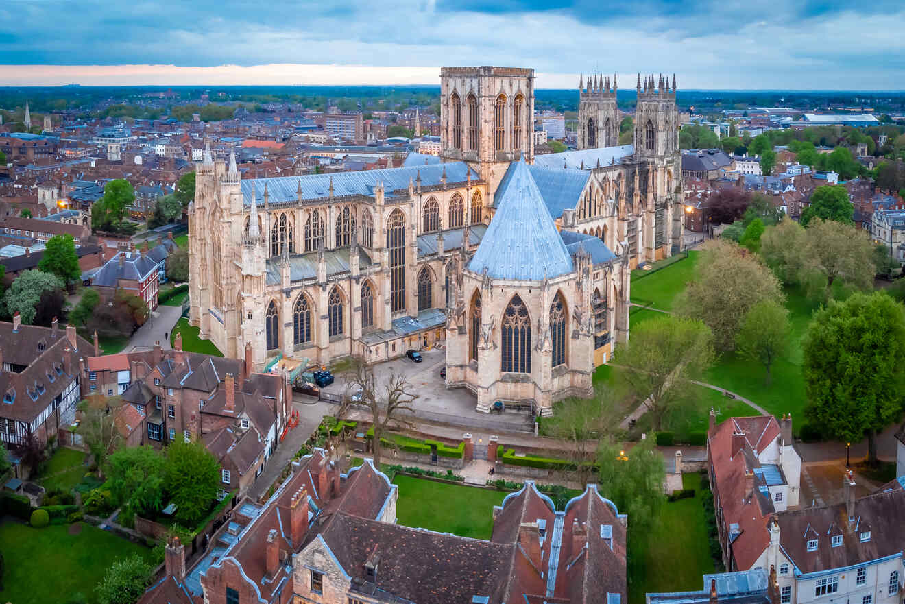 Aerial view of a large Gothic Cathedral with tall towers surrounded by buildings and greenery in a town during daytime.