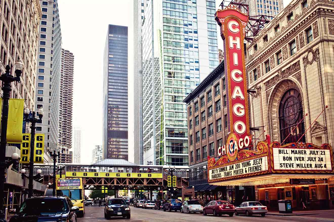 The iconic Chicago Theatre marquee sign glowing in red and yellow, with busy city streets and modern skyscrapers around