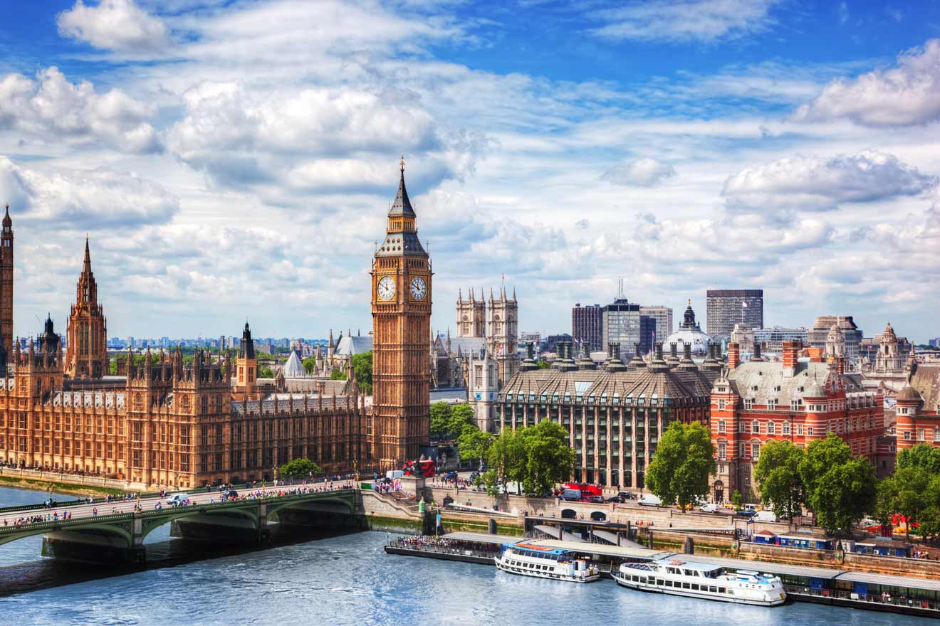 The Houses of Parliament and Big Ben in London, set against a bright blue sky with clouds, viewed from across the River Thames