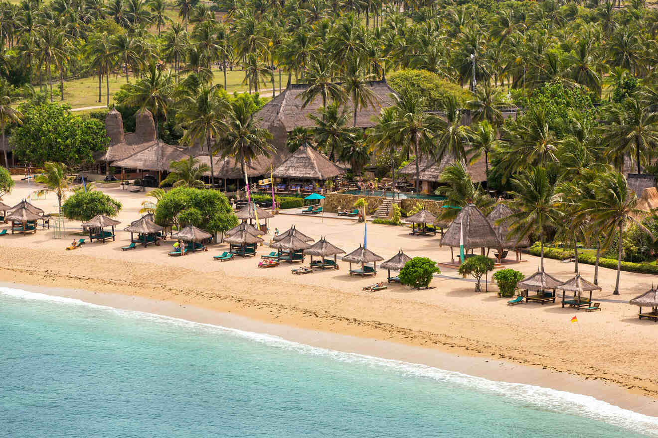 Beach scene with straw umbrellas, loungers, and palm trees near a thatched-roof resort, set along a sandy shoreline with turquoise water.