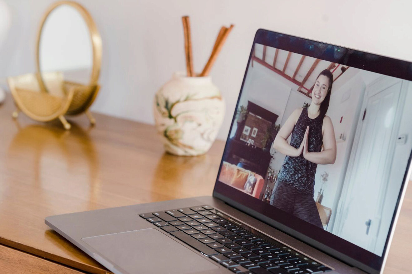 A laptop on a wooden table showing a person in exercise attire performing a yoga pose.