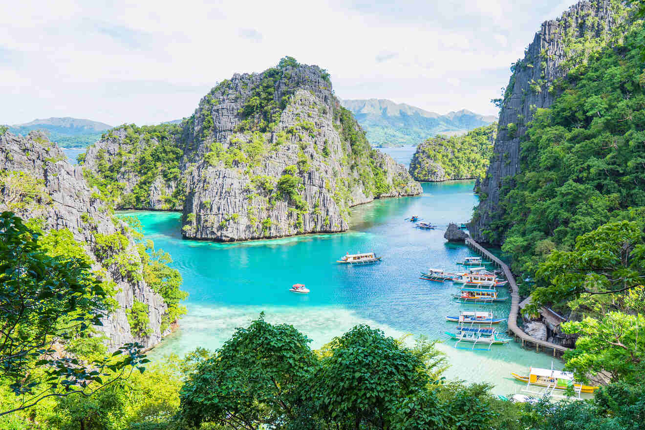 Tropical lagoon with turquoise water, surrounded by rocky cliffs and green vegetation. Several boats are docked near the shore.