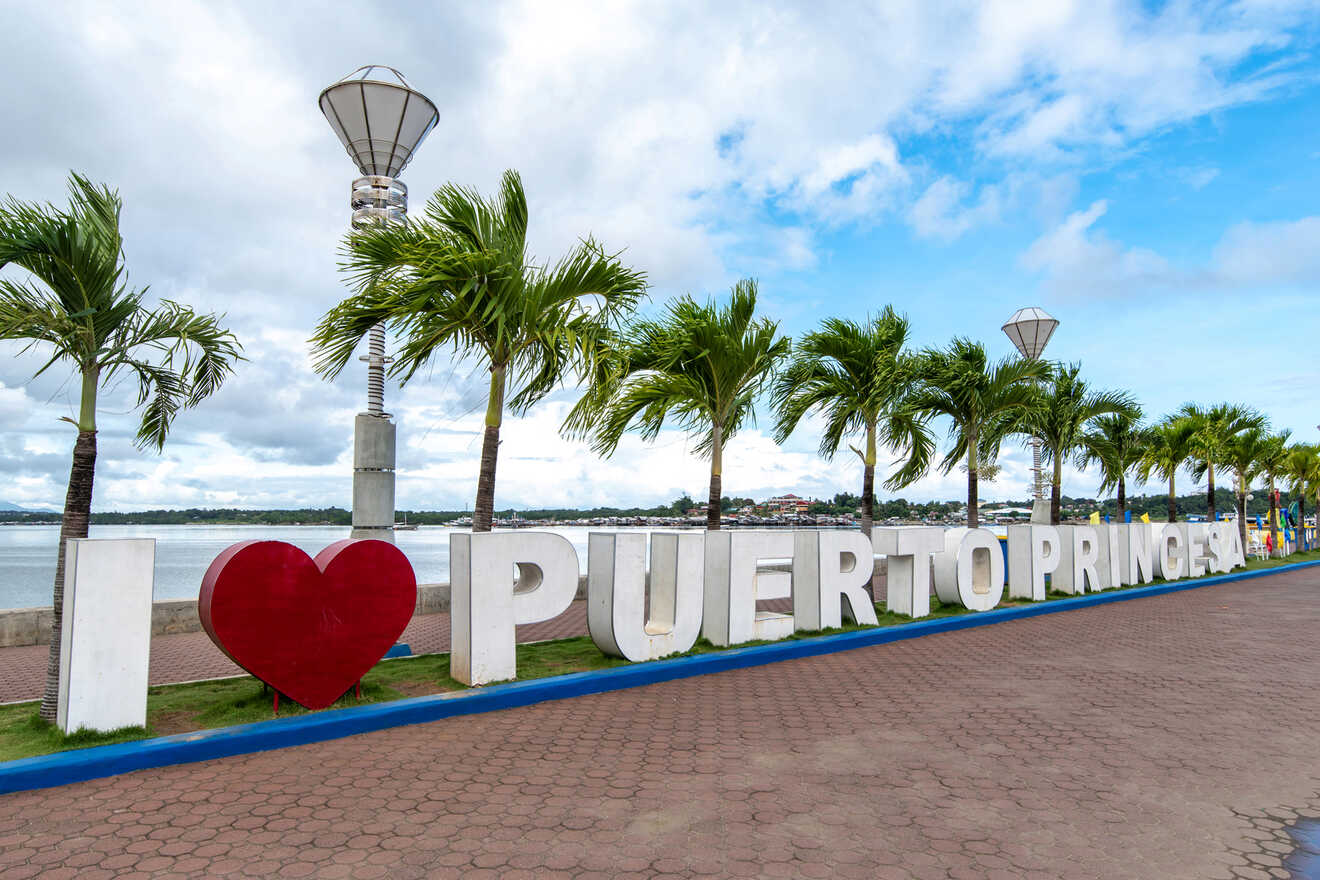 A large sign reads "I ♥ PUERTO PRINCESA" in front of palm trees by the water.