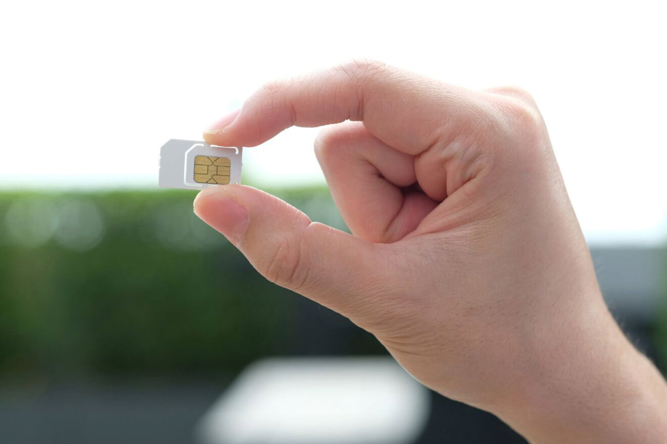 A hand holding a SIM card between the thumb and index finger against a blurred background.